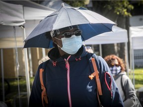 A man protects himself from sun, rain and the coronavirus, while walking along the boardwalk in Sainte-Anne-de-Bellevue.