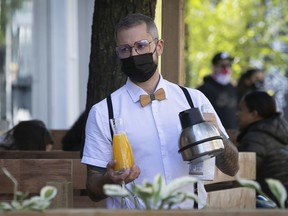 Waiter brings out beverages while tending outdoor tables on Mont-Royal Ave. on Sunday, Sept. 20, 2020.  Quebec Health Minister Christian Dubé is expected to announce later Sunday the COVID-19 alert for Montreal, Quebec City and the Chaudière-Appalaches health regions is being increased to orange (moderate) from yellow (early warning status).