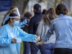 MONTREAL, QUE.: SEPTEMBER 24, 2020 -- Staff from Covid-19 testing centre in Montreal's Park Extension district gives a woman in line a squirt of hand sanitizer Thursday September 24, 2020. (John Mahoney / MONTREAL GAZETTE) ORG XMIT: 65056 - 4395