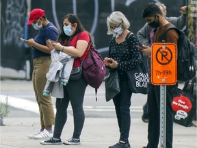 Masked commuters look at their phones while waiting for a bus at the Saint-Laurent métro stop on Sept. 28, 2020.