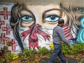 Mechanic Arunasalam Jeyaraj walks by a COVID-19 mask mural on the side of his garage on Marconi St. on Sept. 30, 2020.