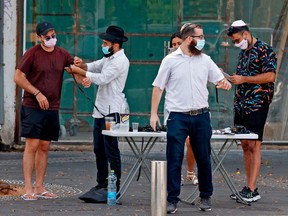 Mask-clad Israeli men bind the tefillin around each other's arms in the coastal city of Tel Aviv on Friday, Sept. 18, 2020.