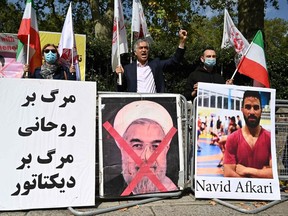 Protesters wave the Lion and Sun flag of the National Council of Resistance of Iran and the white flag of the People's Mujahedin of Iran, two Iranian opposition groups, with a placard depicting the crossed out face of Iran's President Hassan Rouhani as they demonstrate outside the Iranian embassy in London on Saturday, Sept. 12, 2020, against the execution of Iranian wrestler Navid Afkari in the southern Iranian city of Shiraz and against the Iranian government. - Iran said it executed wrestler Navid Afkari, 27, on Saturday at a prison in the southern city of Shiraz over the murder of a public sector worker during anti-government protests in August 2018. Reports published abroad say Afkari was condemned on the basis of confessions extracted under torture, prompting online campaigns of support for his release.