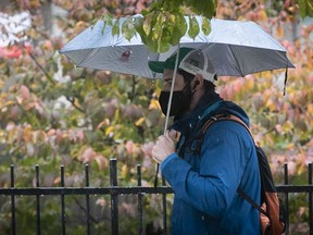 A man walks with his umbrella and mask on Sherbrooke street on Tuesday October 13, 2020.