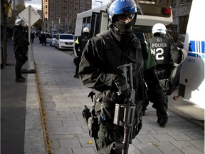 A Montreal police riot squad officer carries a non-lethal launcher to fire tear gas, rubber bullets or gel packets as he stands guard outside the SPVM headquarters during demonstration in Montreal on Saturday, Oct. 24, 2020.