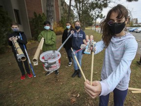 Emma Hlopasko aims her candy slingshot while joining classmates Thomas Gammon, left, Tarun Philip, Sofia Simetic and Olivia Potvin outside Centennial Regional High School in Greenfield Park on Thursday, Oct. 29, 2020.  The students took part in a challenge to design devices that will safely deliver candy for Halloween during the pandemic.