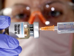 A woman holds a small bottle labeled with a "Vaccine COVID-19" sticker and a medical syringe in this illustration taken April 10, 2020.