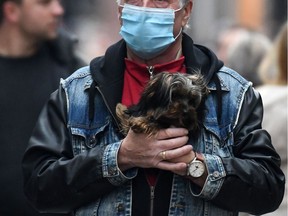 A man wearing a protective face mask carries his dog in the pedestrian area in the city of Dortmund, western Germany, on October 14, 2020.