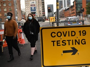 Pedestrians wearing protective face coverings walk past a COVID-19 testing sign in Manchester in northwest England on Saturday, Oct. 17, 2020, as further restrictions come into force as the number of novel coronavirus COVID-19 cases rises. About 28 million people in England, more than half the population, are now living under tough restrictions imposed on Saturday as the country battles a surge in coronavirus cases.