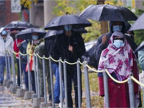 People wait in line in the pouring rain outside a walk-in COVID-19 test clinic in Montreal on Wednesday, Oct. 7, 2020.