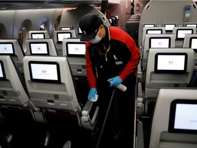 A staff member of Japan Airlines wearing a protective face mask and gloves cleans the cabin of a plane after performing a domestic flight as passengers disembarked at Haneda airport on the first day after the Japanese government lifted the state of emergency, in Tokyo, Japan May 26, 2020.