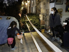 Olivia Mendelssohn gets candy from Joanne Belisle at a home in Montreal West in the Montreal area Saturday, October 31, 2020 during Halloween. Many homes were using safe practices to protect themselves and the visiting children during the pandemic for COVID-19.