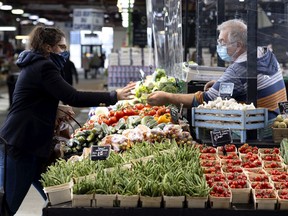 A shopkeeper wears a COVID-19 protective face masks and works behind a plexiglass barrier at the Jean Talon Market on Nov. 12, 2020.