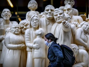 A mask-wearing woman walks past a statue on McGill College Ave. in Montreal Wednesday, November 18, 2020.
