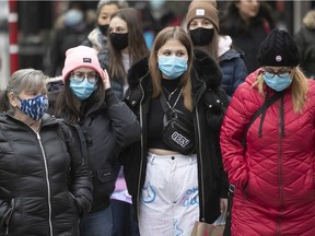 People wearing masks wait at a street light on Ste-Catherine St. on Thursday, Nov. 19, 2020.
