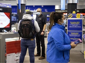 Assistant manger Mohammed speaks with a customer as a greeter waits to help direct others entering the store during the extended Black Friday sales at the downtown Montreal Best Buy store on Nov. 22, 2020.