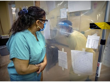 Annie Boto, left, head nurse in the hot zone, speaks with a co-worker through heavy plastic separating the nursing station from the halls at Maimonides.