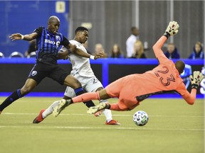 Impact goalkeeper Clément Diop dives to make stop on the New England Revolution’s DeJuan Jones during MLS game at Montreal’s Olympic Stadium on Feb. 29, 2020.