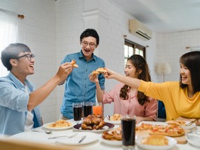 Asia family party eating pizza food and laughing enjoying meal while sitting at dining table together at house.