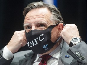 Premier François Legault removes a Montreal Impact mask as he arrives to speak to the media at a COVID-19 press briefing in Montreal on Thursday, Nov. 19, 2020.