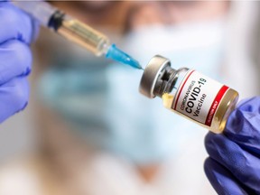 A woman holds a small bottle labeled with a "Coronavirus COVID-19 Vaccine" sticker and a medical syringe in this illustration taken, Oct. 30, 2020.