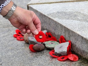 A man places a poppy on the base of the Cross of Sacrifice monument in MacDonald Park in Montreal on Nov. 11, 2020.