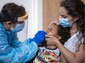 Sonia Egron holds her son Noah as nurse May Joy De Galicia performs a COVID-19 test at the  testing clinic in the Outremont borough of Montreal.