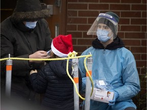 A health worker watches as a man puts a face mask on a child at a COVID-19 testing site on Parc Ave. on Monday, Nov. 30, 2020.