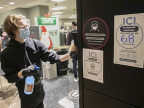 A store clerk washes walls near signs that indicate the number of clients allowed inside a store at the Complexe Dejardins in December 2020.