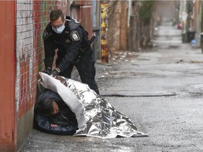 A Montreal police officer places a thermal blanket on a homeless woman sleeping in a lane off Rachel St.