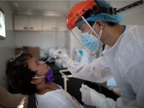 A nurse gets a swab from a man under observation for COVID-19 in a booth set up in a hospital parking lot in Manila.