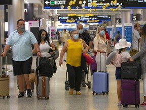 Travellers wearing protective face masks walking through Concourse D at the Miami International Airport on Sunday, Nov. 22, 2020, in Miami, Fla.
