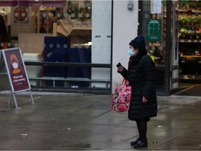 A woman wearing a face mask waits for a bus outside a supermarket as EU countries impose a travel ban from the UK amid alarm about a rapidly spreading strain of coronavirus, in Fulham, London, Britain, December 21, 2020.   REUTERS/Kevin Coombs