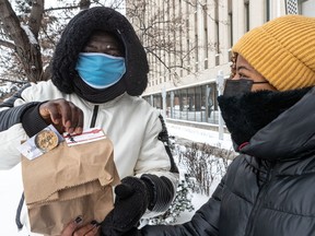 Kristina Dejean, right, of the community group Je me souviendrai, hands traditional Haitian joumou soup to Mamadou Konaté, a 39-year-old asylum seeker who contracted COVID-19 while working in a CHSLD, in front of Prime Minister Justin Trudeau's offices in Montreal on Saturday, Jan. 2, 2021.