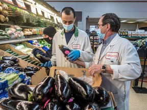 Manager Jacques Lecavalier, right, and employee Mohamed Weddah stock the vegetable aisle at the Esposito grocery store in Montreal on Friday, Jan. 8, 2021.