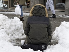A person panhandles on Ste-Catherine St. in Montreal after clearing snow for a place to sit.