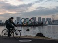 A man wearing a face mask cycles past the Olympic Rings on Friday, Jan. 22, 2021, in Tokyo.