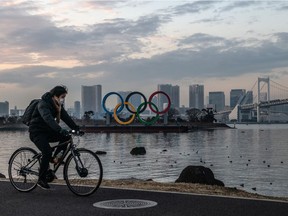 A man wearing a face mask cycles past the Olympic Rings on Friday, Jan. 22, 2021, in Tokyo. With only six months to go until the start of the Games, it has been reported the Japanese authorities have privately concluded the Olympics could not proceed because of the continuing COVID-19 coronavirus pandemic. Spokespersons from the IOC and Japanese government have since rejected the report.