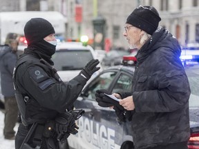 A man talks with a police officer after being issued a fine during a demonstration in Montreal, Sunday, Dec. 20, 2020, protesting measures implemented by the Quebec government to help stop the spread of COVID-19.
