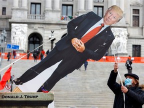 An anti-Trump protester pulls a cardboard cutout depicting U.S. President Donald Trump as his supporters are expected to protest against the election of President-elect Joe Biden, outside the Pennsylvania State Capitol in Harrisburg, Pa., on Sunday, Jan. 17, 2021.