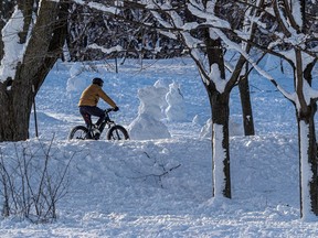 The setting sun casts shadows on the weekend snowfall on Mount Royal as a cyclist passes by in Montreal on Monday January 18, 2021.