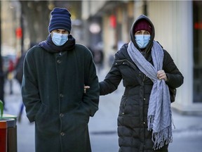 A mask-wearing couple walk down Saint-Catherine St. in Montreal.
