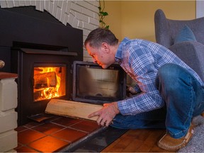 Ste-Anne-de-Bellevue city councillor Ryan Young puts another log in his wood-burning stove. He recently fitted it with an insert to meet new cleaner bylaw standards.