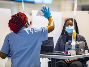 A worker disinfects a plexiglass divider at one of the registration kiosks at the COVID-19 testing centre on the arrivals level at Montreal's Trudeau airport, Feb. 21, 2021.