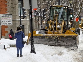 A woman waits while a tractor clears snow off the sidewalk on Prince Arthur St. on Feb. 5, 2021.