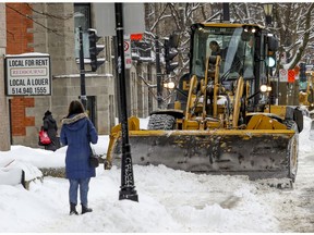 A woman waits while a tractor clears snow off the sidewalk on Prince Arthur St. in Montreal Friday February 5, 2021.