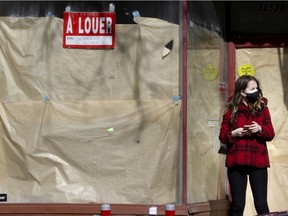 MONTREAL, QUE.: February 26, 2021 -- A woman stops to check her phone in front of a shuttered store on Saint-Laurent St. in Montreal Feb. 26, 2021.