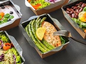 Ready healthy food catering menu in lunch boxes fish and vegetable packages as daily meal diet plan courier delivery with fork isolated on black table background. Take away containers order concept.