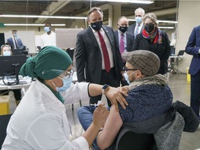 Premier François Legault watches a man get his COVID-19 vaccine at a clinic in Montreal's Olympic Stadium on Tuesday, February 23, 2021.