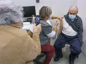 Maria Levita photographs her husband, Bruno, receiving his first dose of COVID-19 vaccination in Laval on Thursday, Feb. 25, 2021, marking the start of mass vaccination in Quebec.